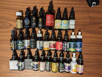 Various cannabis tincture bottles with dropper caps placed on a natural wood surface surrounded by green leaves.