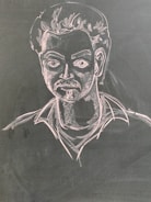 A chalk drawing depicting a man with stylized facial features including a mustache and voluminous hair. The figure is drawn on a dark surface with light detailing that highlights the contours and expressions.