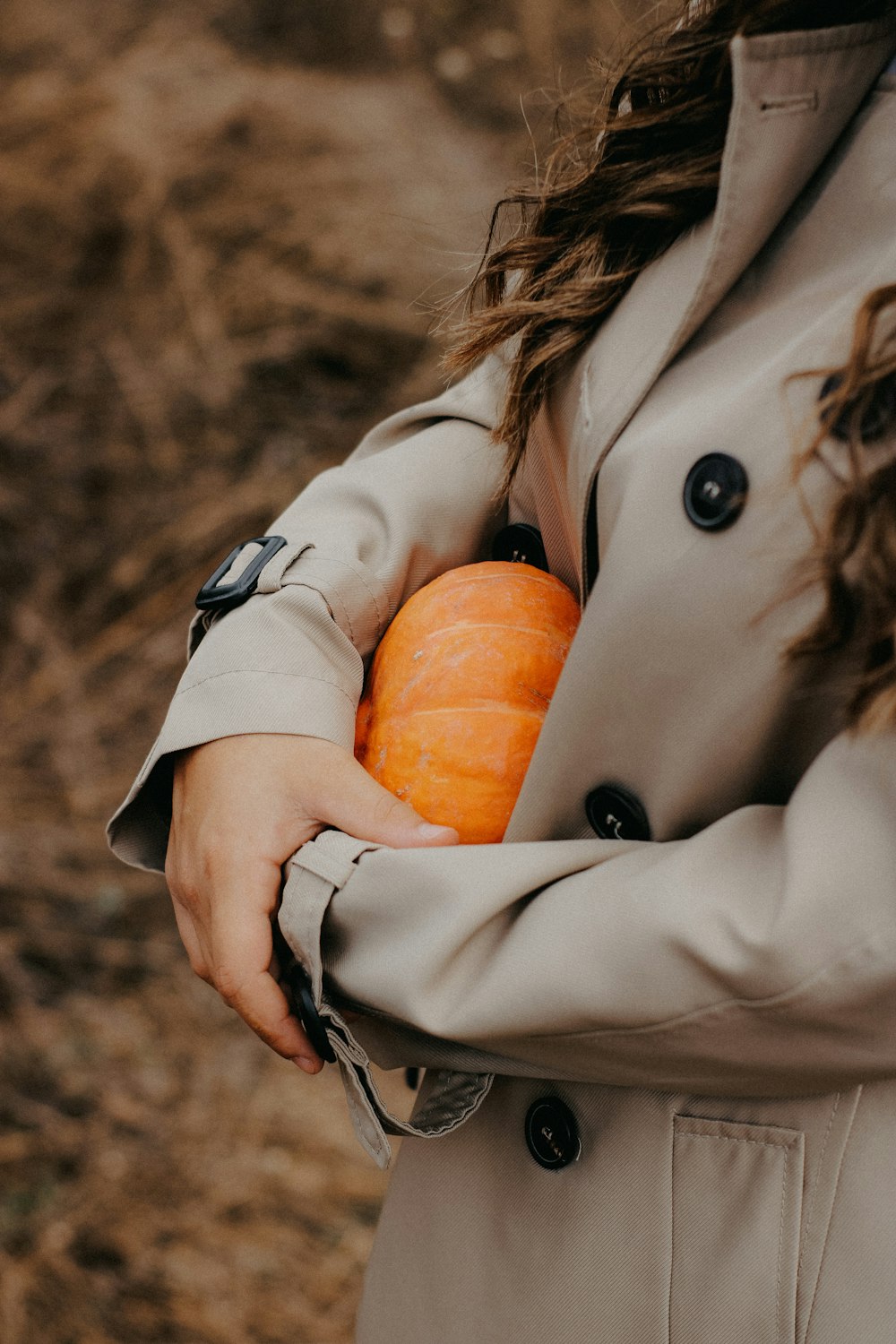 a woman in a trench coat holding a pumpkin