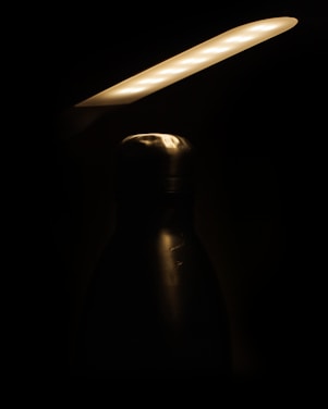 A close-up shot of a sleek wine bottle glistening under soft, warm lighting on a minimalist white surface.