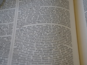 A close-up view of a page from a Bible, featuring text laid out in two columns. The focus is sharp on a section of verses, with surrounding text slightly blurred. The page is open, with part of another page visible, suggesting depth and context.