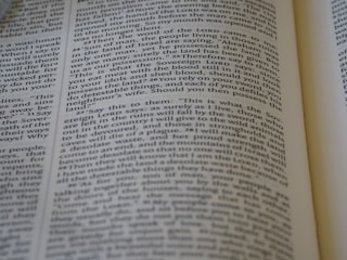 A close-up view of a page from a Bible, featuring text laid out in two columns. The focus is sharp on a section of verses, with surrounding text slightly blurred. The page is open, with part of another page visible, suggesting depth and context.