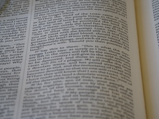 A close-up view of a page from a Bible, featuring text laid out in two columns. The focus is sharp on a section of verses, with surrounding text slightly blurred. The page is open, with part of another page visible, suggesting depth and context.