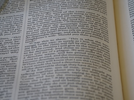 A close-up view of a page from a Bible, featuring text laid out in two columns. The focus is sharp on a section of verses, with surrounding text slightly blurred. The page is open, with part of another page visible, suggesting depth and context.