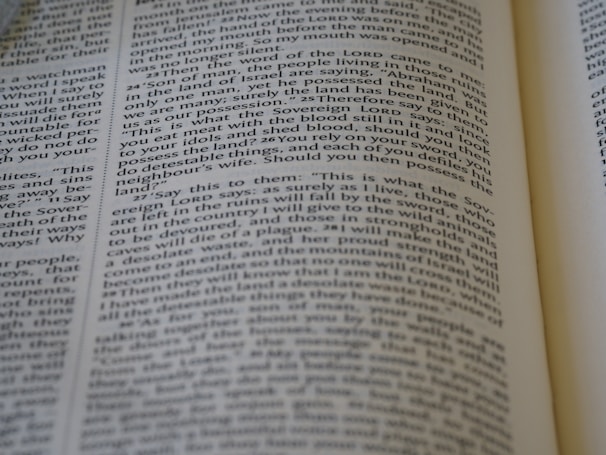 A close-up view of a page from a Bible, featuring text laid out in two columns. The focus is sharp on a section of verses, with surrounding text slightly blurred. The page is open, with part of another page visible, suggesting depth and context.