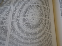 A close-up view of a page from a Bible, featuring text laid out in two columns. The focus is sharp on a section of verses, with surrounding text slightly blurred. The page is open, with part of another page visible, suggesting depth and context.