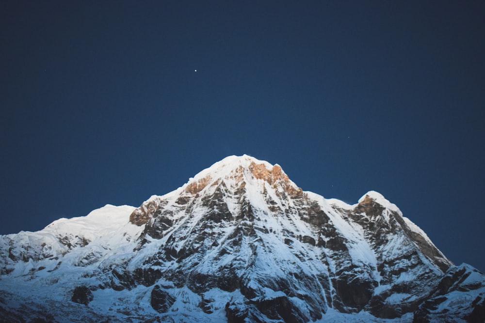 the top of a snow covered mountain under a blue sky