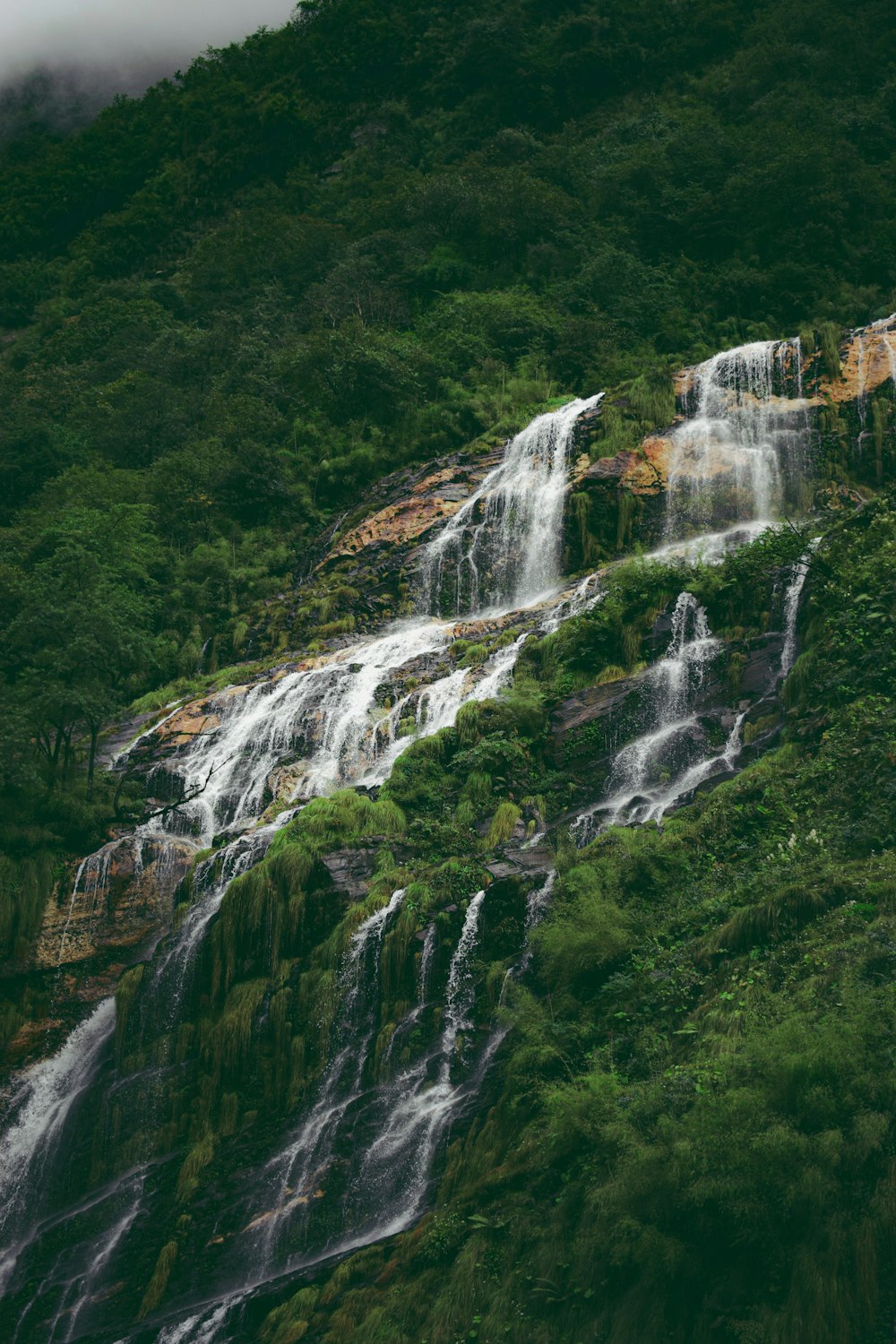 a very tall waterfall in the middle of a lush green hillside