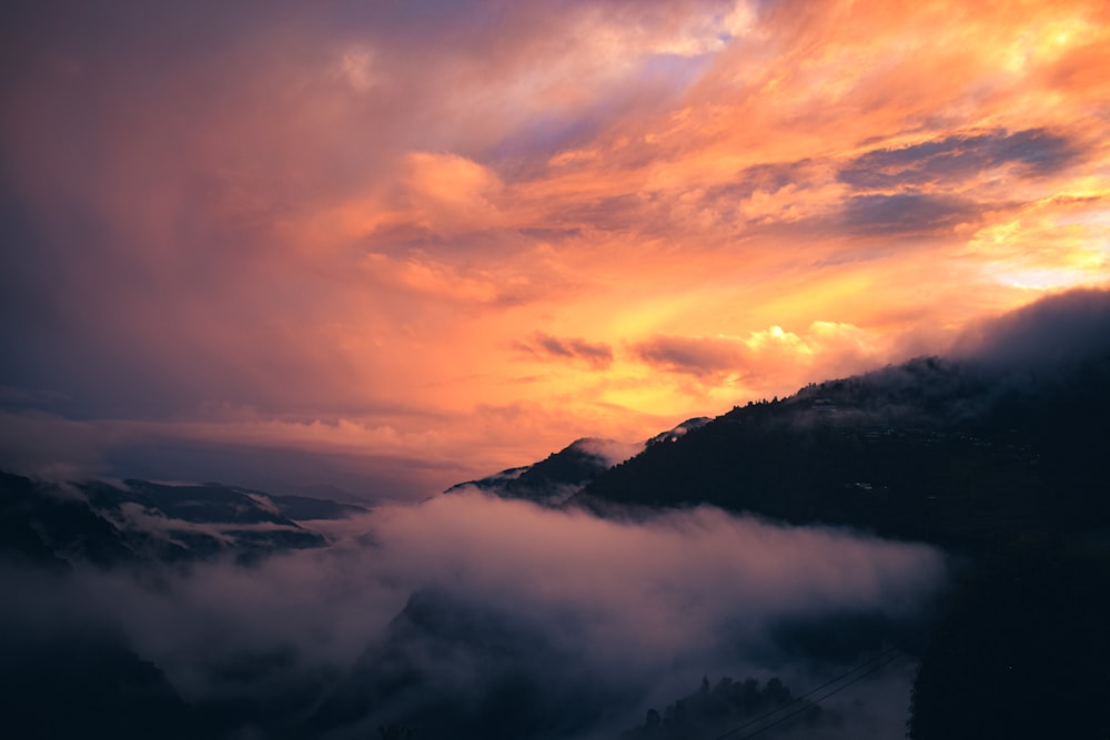 a view of a mountain covered in clouds at sunset