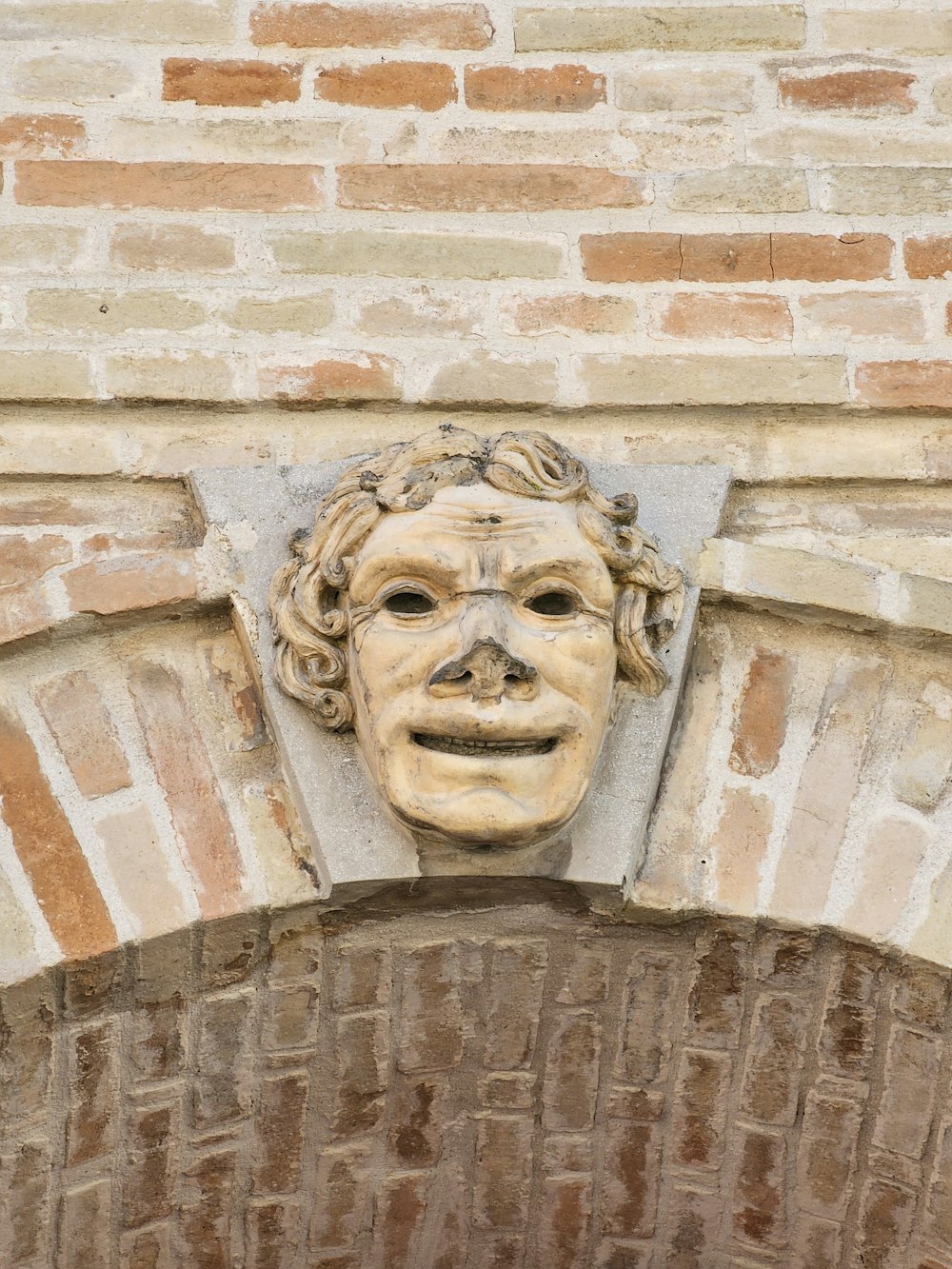 eine Statue des Gesichts eines Mannes auf einer Ziegelmauer