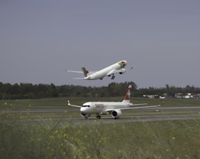 two airplanes are flying low over a runway