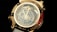 A luxury watch features intricate detailing with a prominent globe design on its face. The numerals and watch hands are elegantly integrated, surrounded by a metallic gold casing. There are engraved words and numbers on the case, and the visible strap is white.