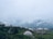 A picturesque mountain landscape with several dome-shaped structures and tents nestled among lush greenery. Mist and clouds hover low in the sky, creating a serene and tranquil atmosphere.