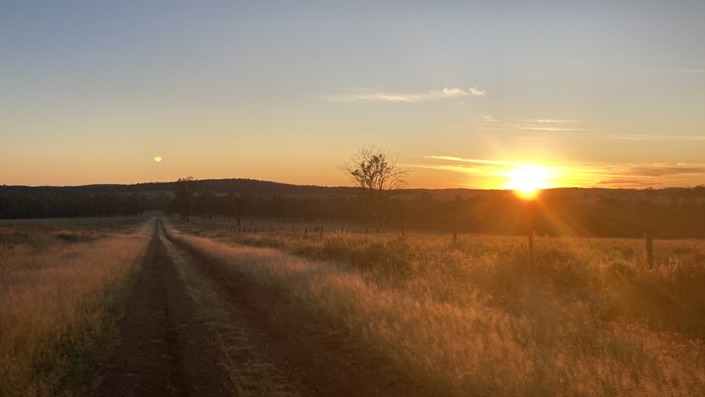 the sun is setting over a dirt road