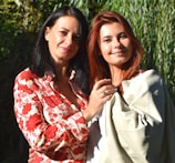 two women standing next to each other in front of trees