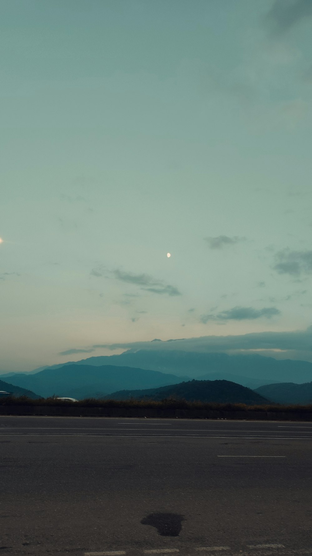 a view of a mountain range at dusk with the moon in the sky