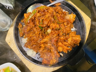A sizzling pan with vegetables and meat glazed in hot pepper cool sauce.