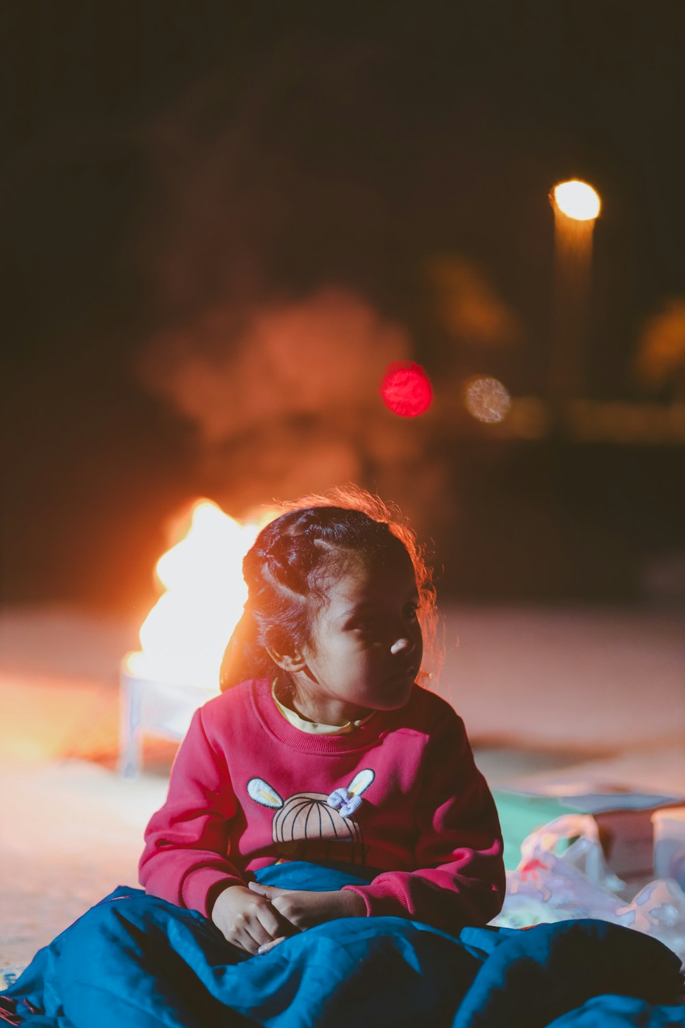 a little girl sitting on the ground in front of a fire