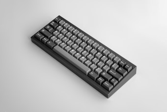 A mechanical keyboard with a minimalist design, featuring a compact layout and a mix of dark gray and light gray keycaps. The keys are arranged in several rows and columns, and the keyboard has a sleek, modern appearance.