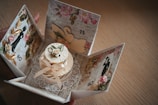 A beautifully crafted card box with an intricate design, featuring floral patterns and silhouettes of elegant figures. The center showcases a small decorative cake adorned with ribbons and a flower, surrounded by a lace-like embellishment.