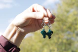 Hand holding a pair of sleek, modern earrings against a blurred LA cityscape.