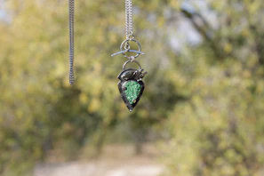 Sophisticated gold and gemstone pendant hanging against a blurred background of lush greenery