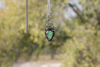 A sparkling diamond pendant hanging from a fine chain against a blurred garden background.