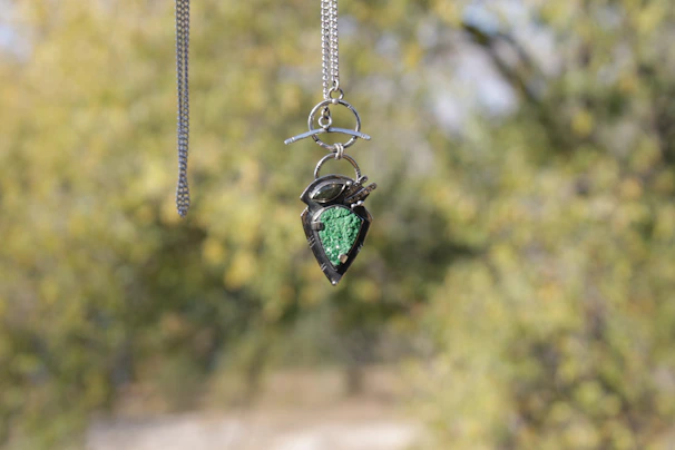 A sparkling diamond pendant hanging from a fine chain against a blurred garden background.