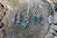 Several pieces of jewelry, including earrings and a necklace with green stones, are placed on a weathered tree stump. The jewelry has metal fittings, giving it a rustic and elegant look.