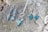 A collection of silver jewelry, including a pair of earrings and a necklace with geometric designs and green stones, is displayed on a textured wooden surface.