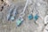 A collection of silver jewelry, including a pair of earrings and a necklace with geometric designs and green stones, is displayed on a textured wooden surface.