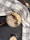 A bowl of oatmeal topped with banana slices, blackberries, nuts, and seeds is placed on a table. A white and gray checkered cloth is draped around it. Adjacent to the bowl, there is a wooden spoon with scattered oats.
