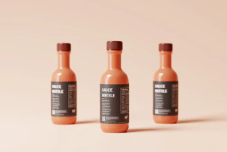 Close-up of sleek hot sauce bottles with minimalist labels in off-white and charcoal, arranged on a warm gray backdrop.