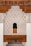 Intricate architectural design featuring detailed geometric and floral patterns carved into plaster, set against a backdrop of rich, dark wood. The design includes an arch with an ornate lattice window. Arabic calligraphy runs along the top edge, adding a cultural and historical dimension.
