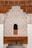 Intricate architectural design featuring detailed geometric and floral patterns carved into plaster, set against a backdrop of rich, dark wood. The design includes an arch with an ornate lattice window. Arabic calligraphy runs along the top edge, adding a cultural and historical dimension.