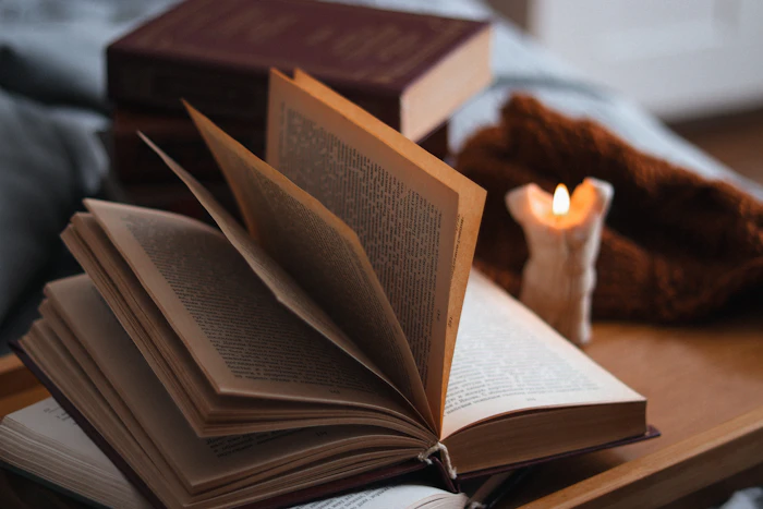 An open book on a wooden table beside a softly lit candle