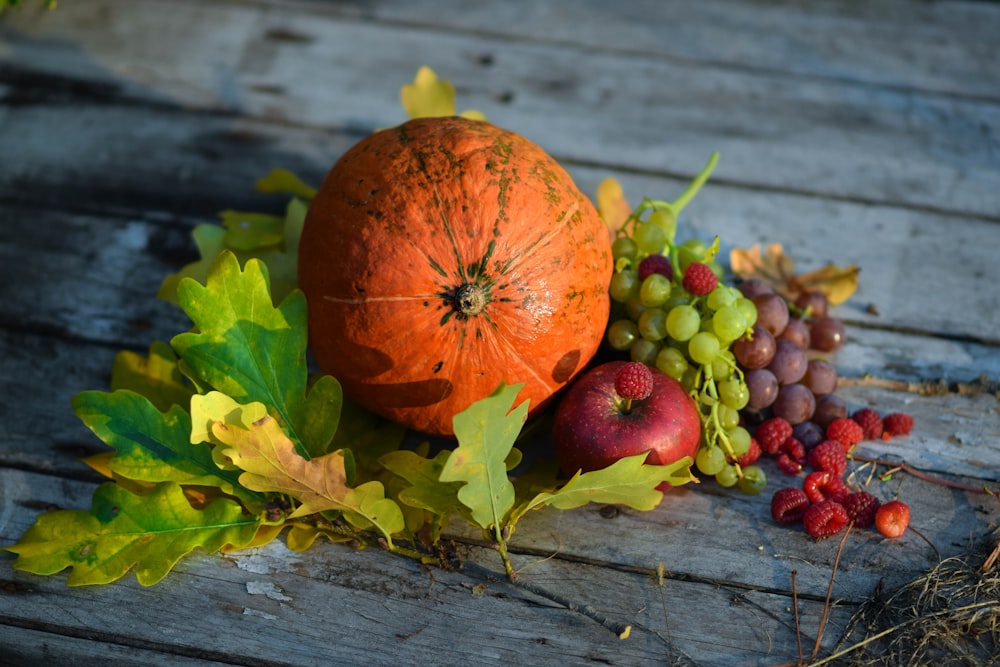 a pumpkin, grapes, and leaves on a wooden table