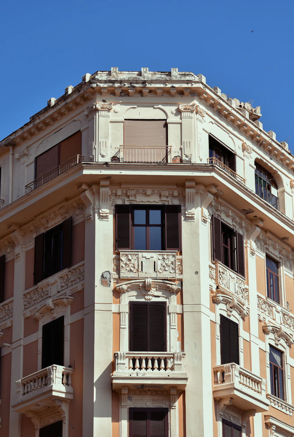 The image shows a tall, ornate building with multiple levels and balconies. The building is painted white with accents of orange and brown, giving it an elegant appearance. The top level features a large window that allows for natural light to enter the interior. The balconies on each floor are adorned with intricate carvings and statues, adding to the overall aesthetic appeal of the structure.