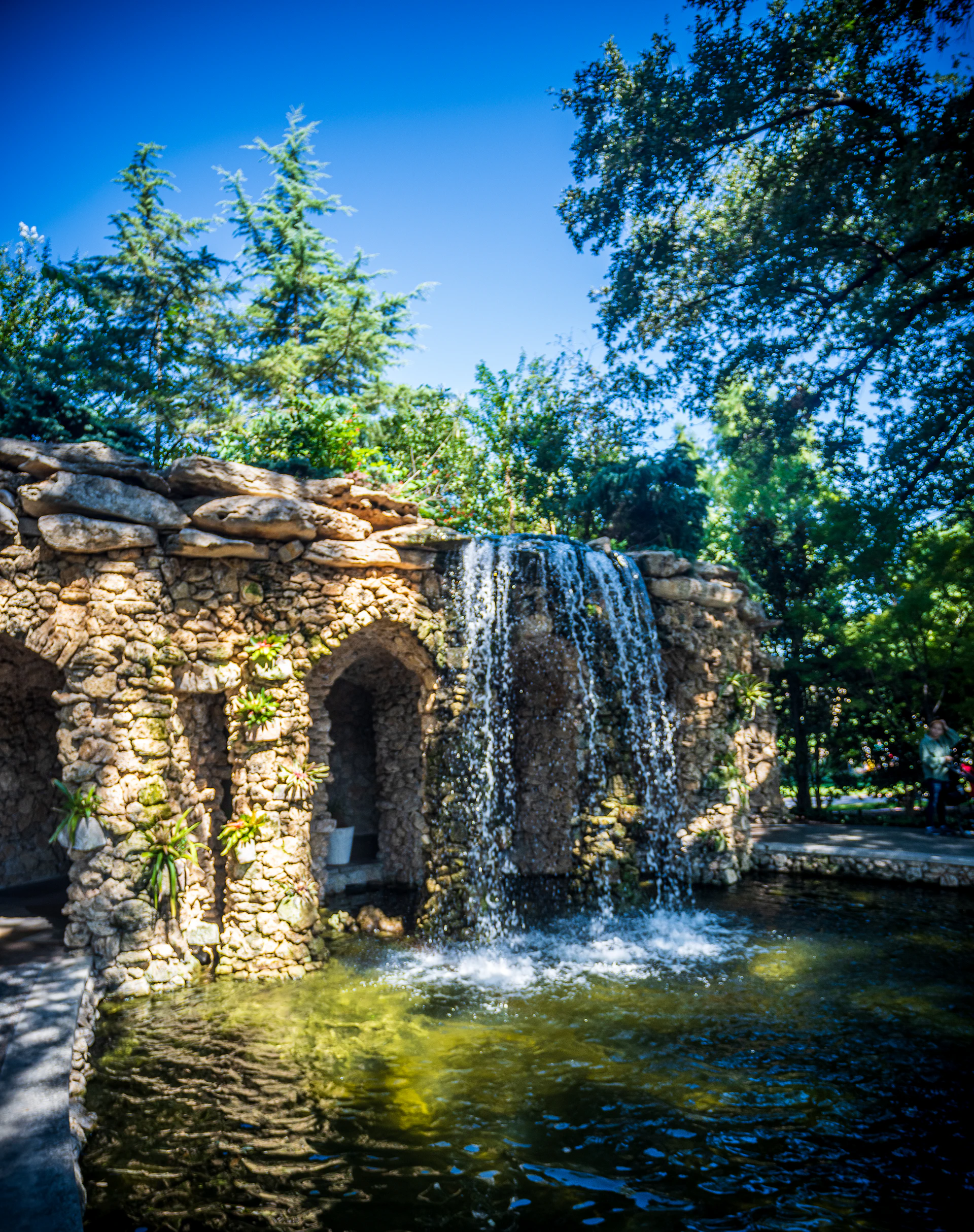 A serene backyard waterfall cascading over natural stones into a crystal-clear pond, surrounded by lush greenery.