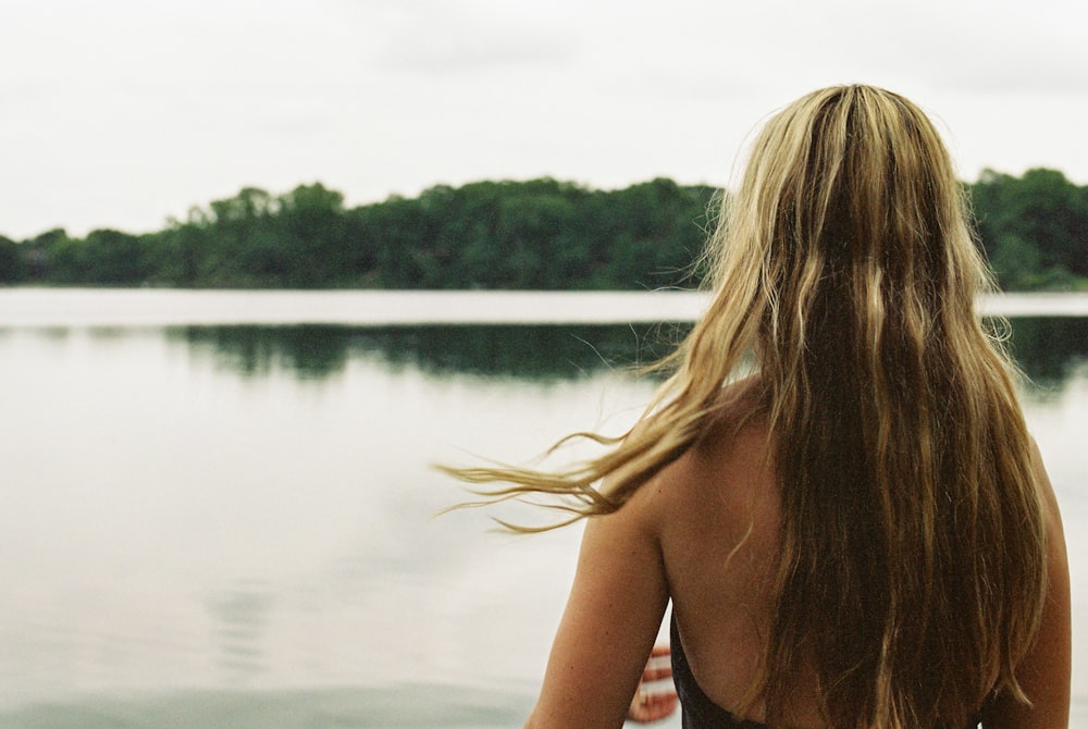 a woman with long hair standing by a lake