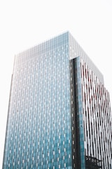 A modern high-rise building with a facade of blue-tinted glass panels and vertical brown accents. The building's surface reflects the light, creating a sleek and contemporary architectural appearance.