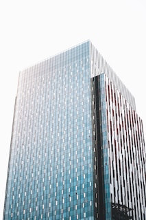 A modern high-rise building with a facade of blue-tinted glass panels and vertical brown accents. The building's surface reflects the light, creating a sleek and contemporary architectural appearance.