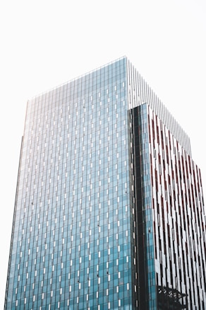 A modern high-rise building with a facade of blue-tinted glass panels and vertical brown accents. The building's surface reflects the light, creating a sleek and contemporary architectural appearance.