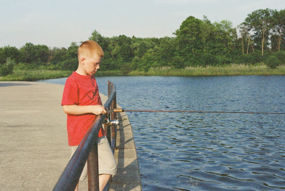 a young boy standing on a pier next to a body of water