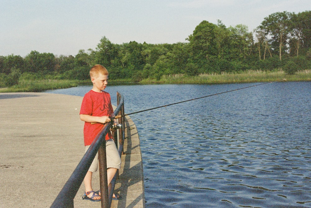 a young boy standing on a pier next to a body of water
