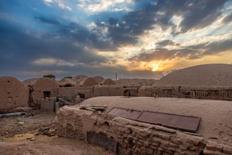 A traditional mud-brick house in Mali surrounded by baobab trees under a golden sunset.