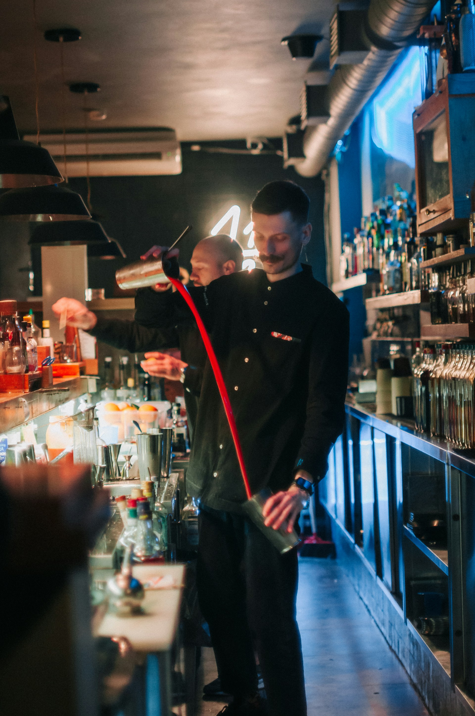 Close-up of a bartender expertly preparing a shot with vibrant ingredients under warm lighting.