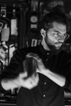 A friendly bartender smiling while holding a cocktail shaker in a cozy home bar setting.