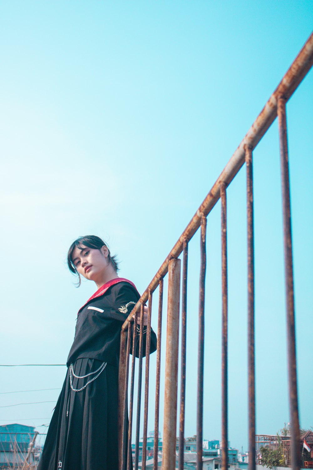 a woman in a black dress leaning on a fence