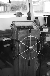 A vintage-looking ship's helm station with a wooden steering wheel and gauges. The interior has a rustic feel and includes communication equipment like a radio.